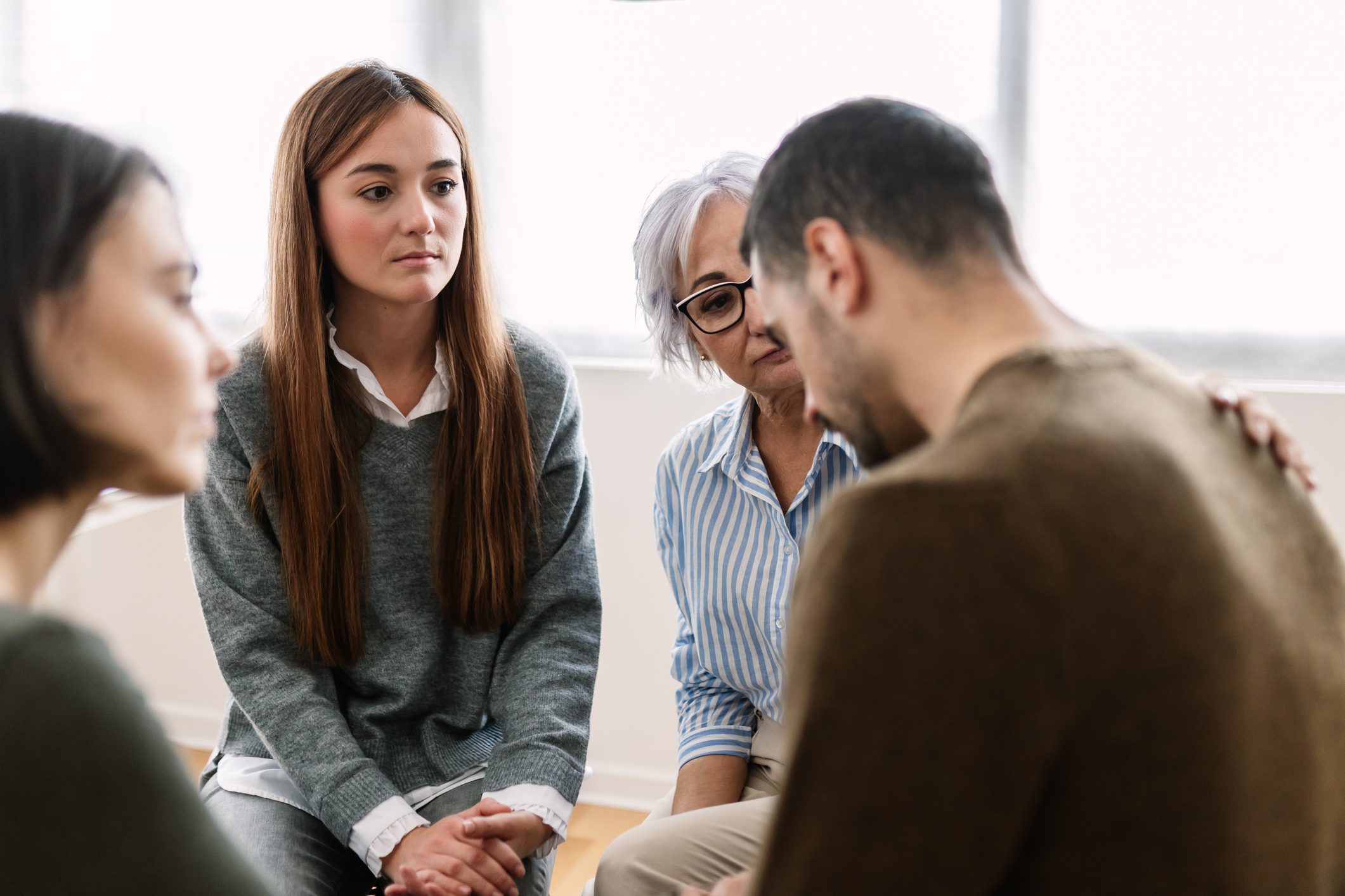 Small group of adults comfort a downcast man during group therapy