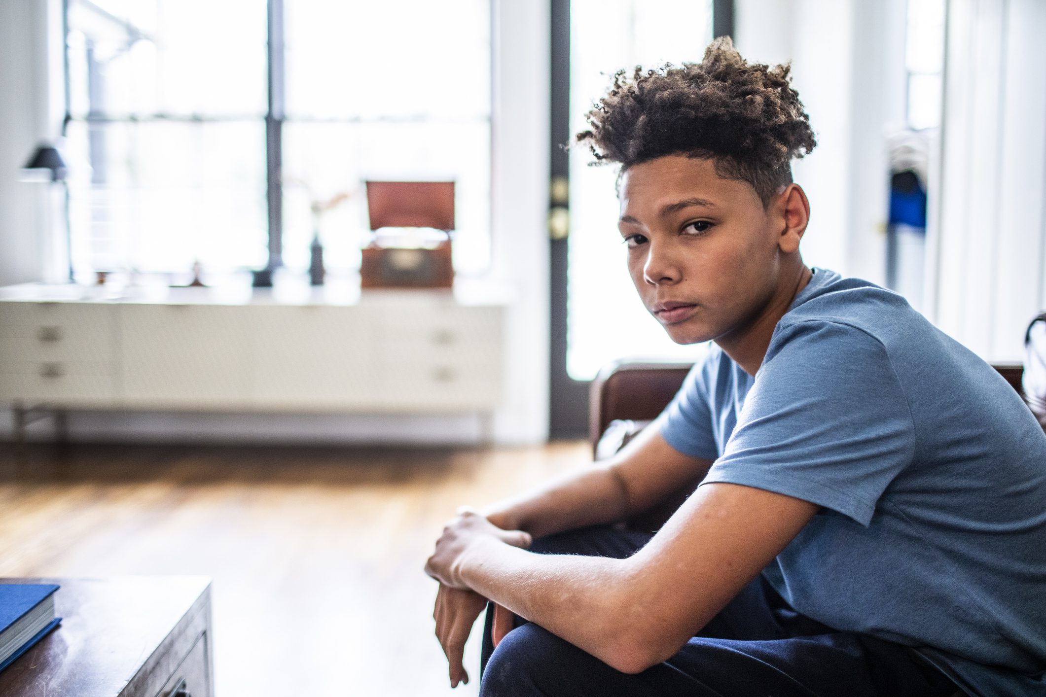 Hopeless teen boy sits at the edge of the sofa in his home