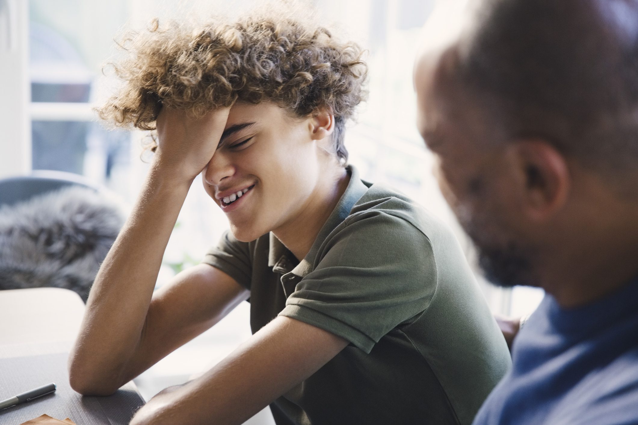 Frustrated teenage boy holds his hand to his head while his father looks toward him.