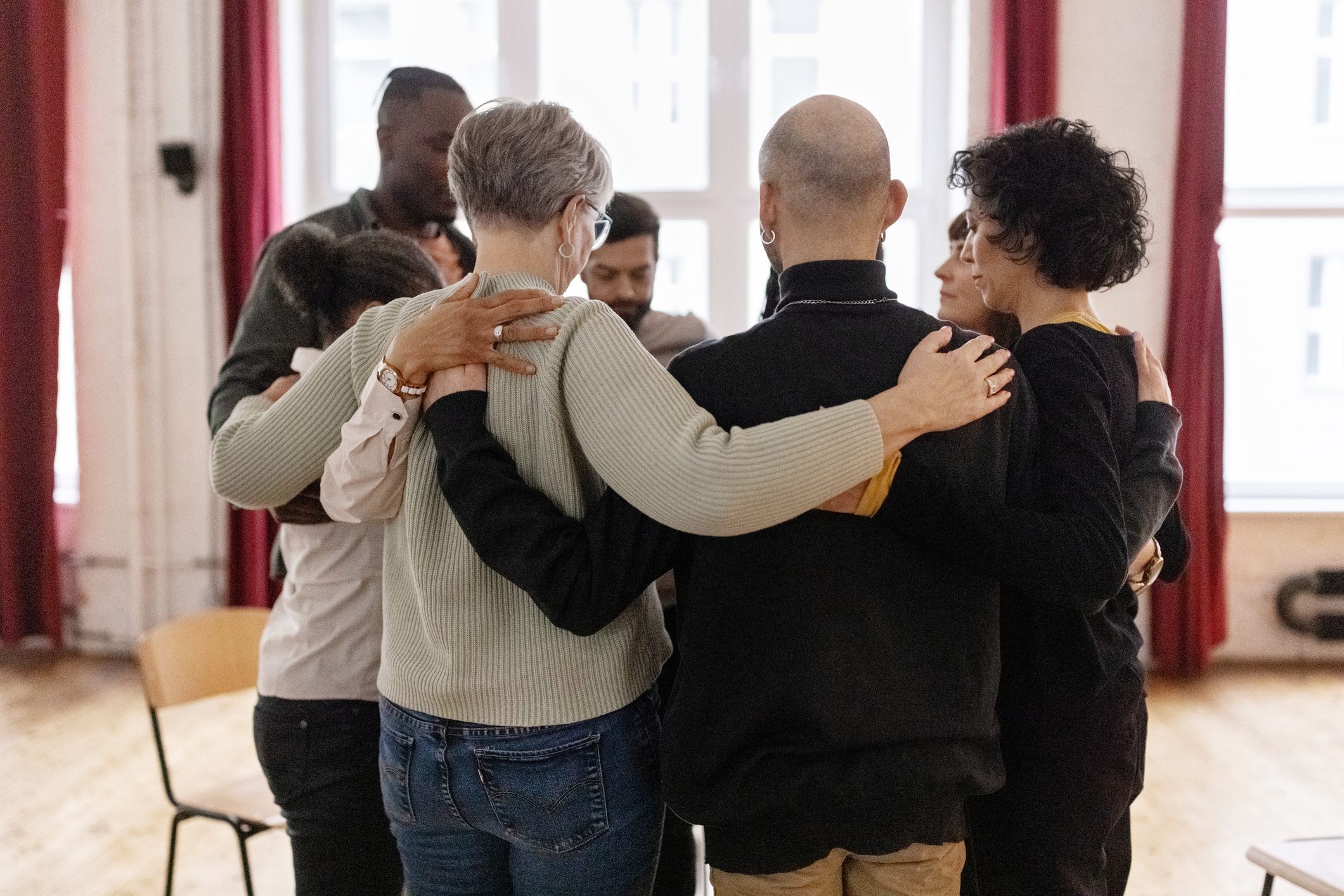 A group of adults hug each other in a circle during group therapy.
